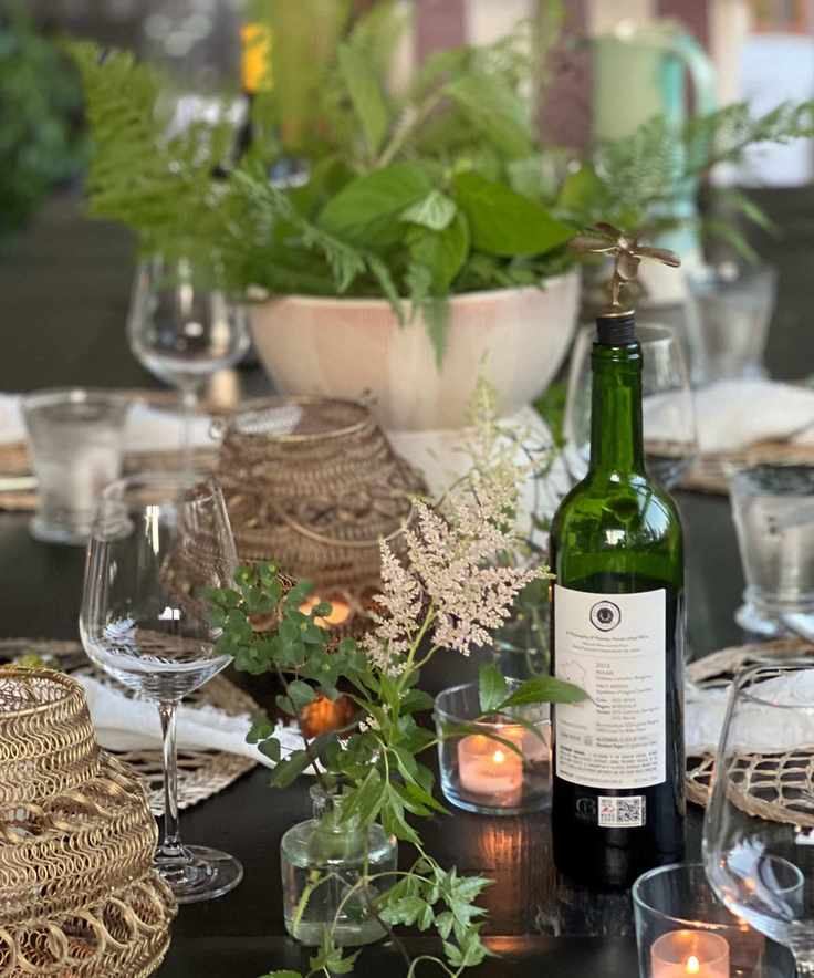 table set with rattan placemats, glassware and greenery in a central bowl and small glass vases