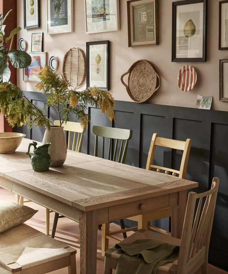 Dining room with pale pink walls and black paneling, featuring a wall of frames and decor, light wood dining table with assorted chairs