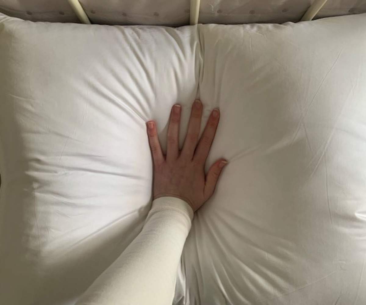 A hand pressing down on the Brooklinen Down Pillow.