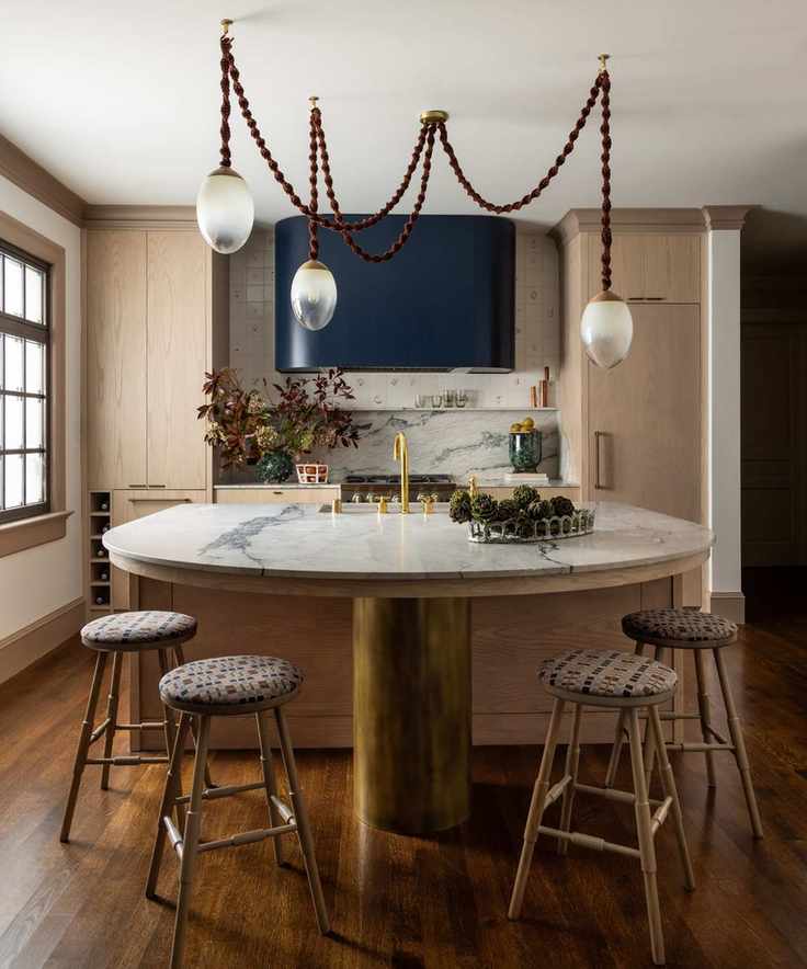 A wooden kitchen with marble countertops and a statement light fixture featuring dark purple hues and frosted glass