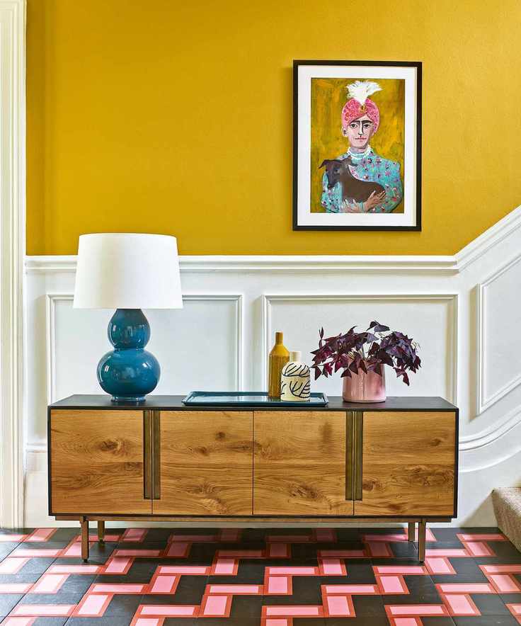 Yellow entryway with colorful floor, white wall panels and wood console