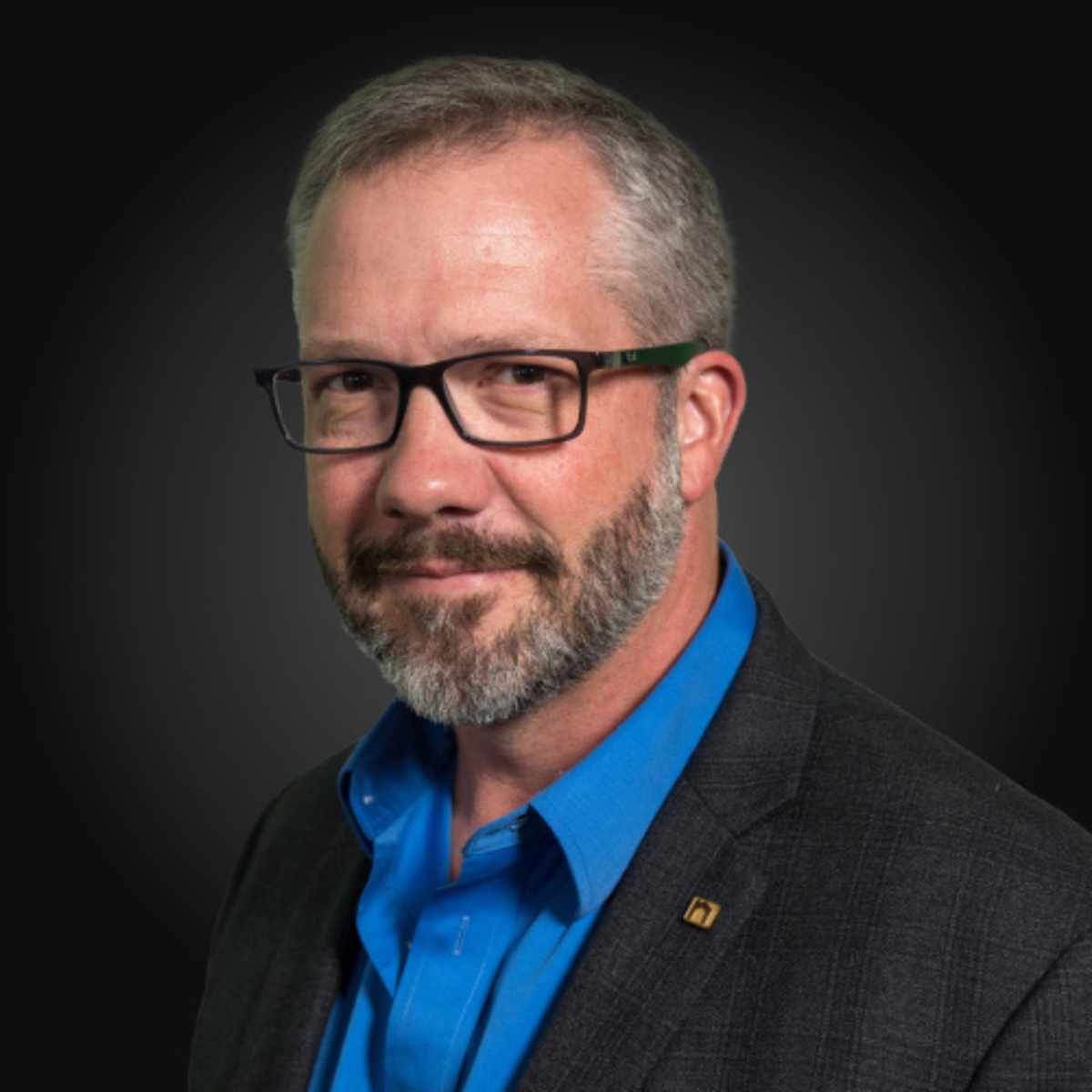 A headshot of Matt Kunz – a man wearing glasses, a black blazer, and a blue shirt, in front of a black background