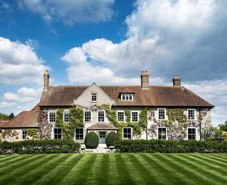 An example of front garden ideas showing a large country home with a neat lawn, low level hedging and ivy on the house