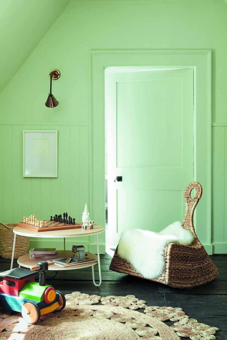 playroom with green walls rattan rocking chair, round table, wall light, tory train, black floorboards, rug