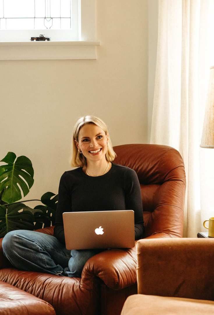 Woman working on laptop in cozy armchair.