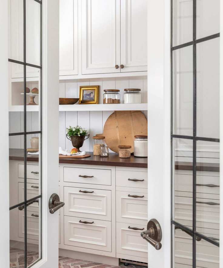 A white pantry with black countertops decorated with a wood cutting board