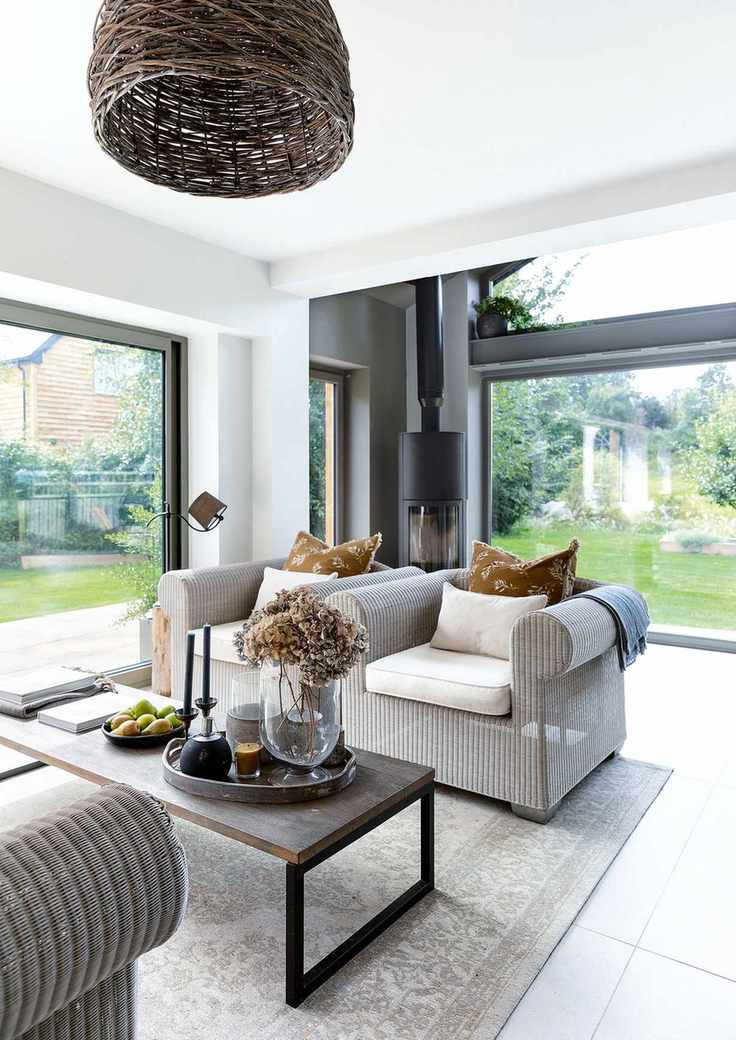 rattan style sofa and coffee table in room with full height glass windows with woodburning stove behind