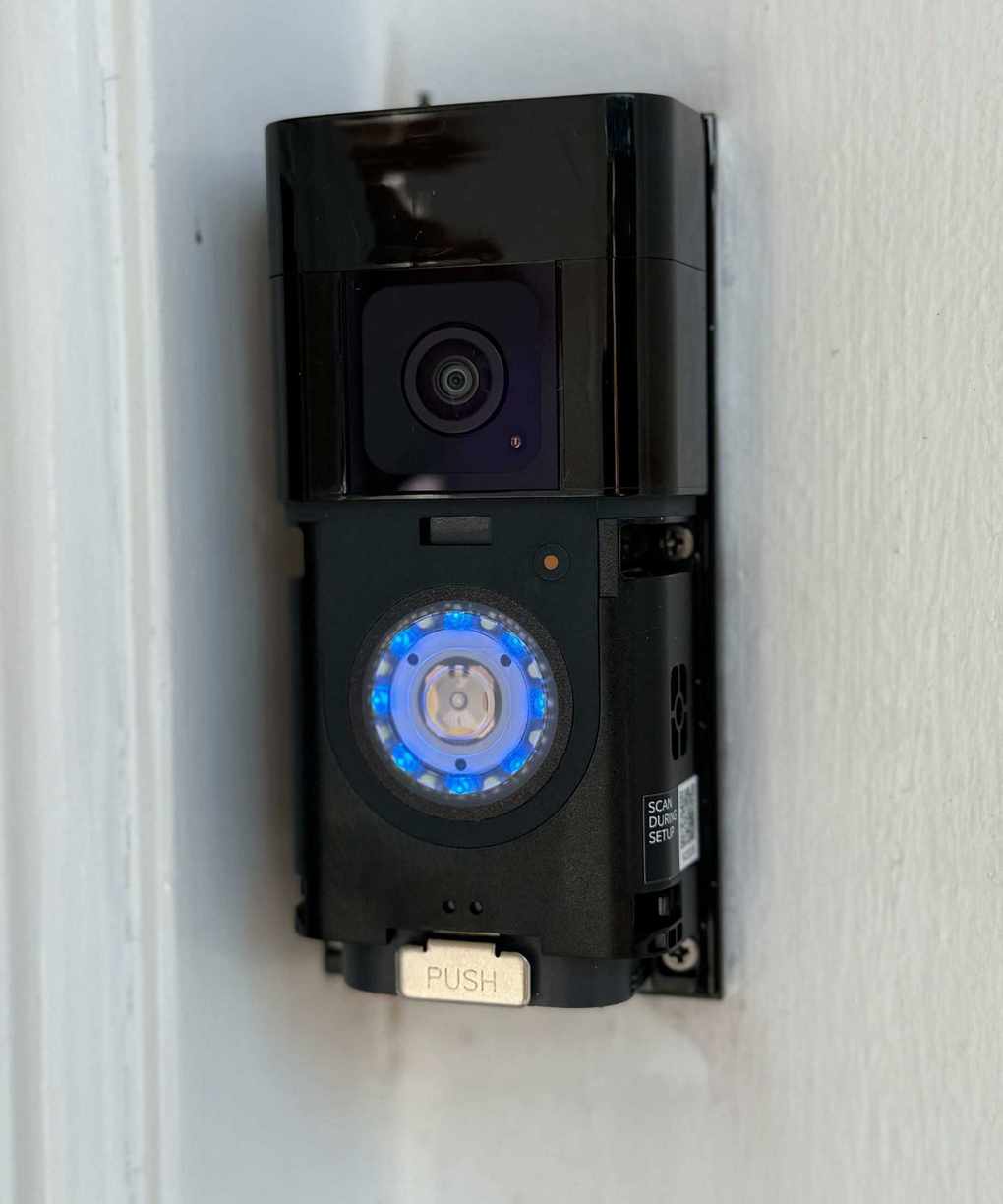 A black Ring Battery Doorbell Plus with the faceplate removed, mounted on a white wall
