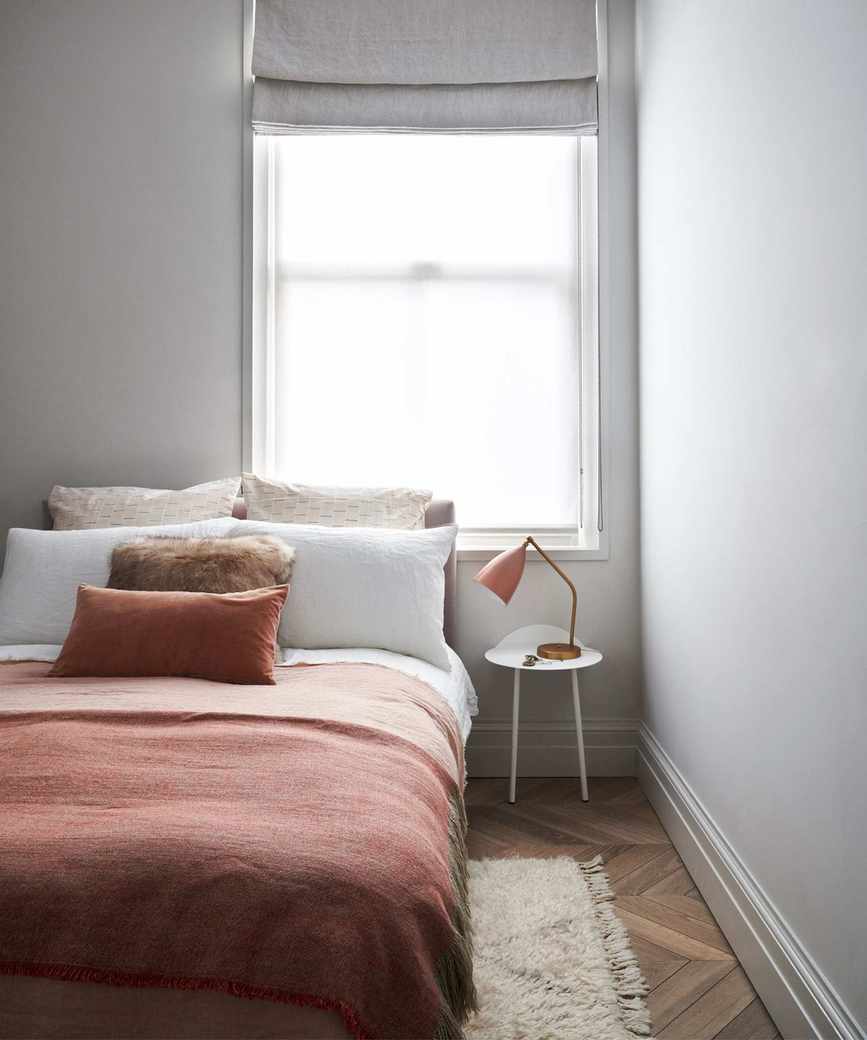 Bedroom with double bed with brown and white bedding beside sash window with grey blinds, wooden flooring.
