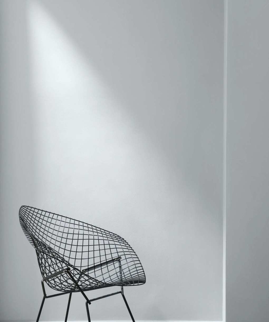 A wall painted in a cool grey, with a black metal chair sitting in front of it.