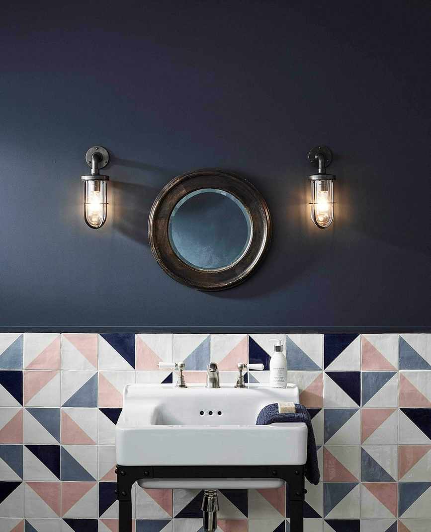 A navy bathroom with a white sink in front of colored wall tiles in blue, pink and white