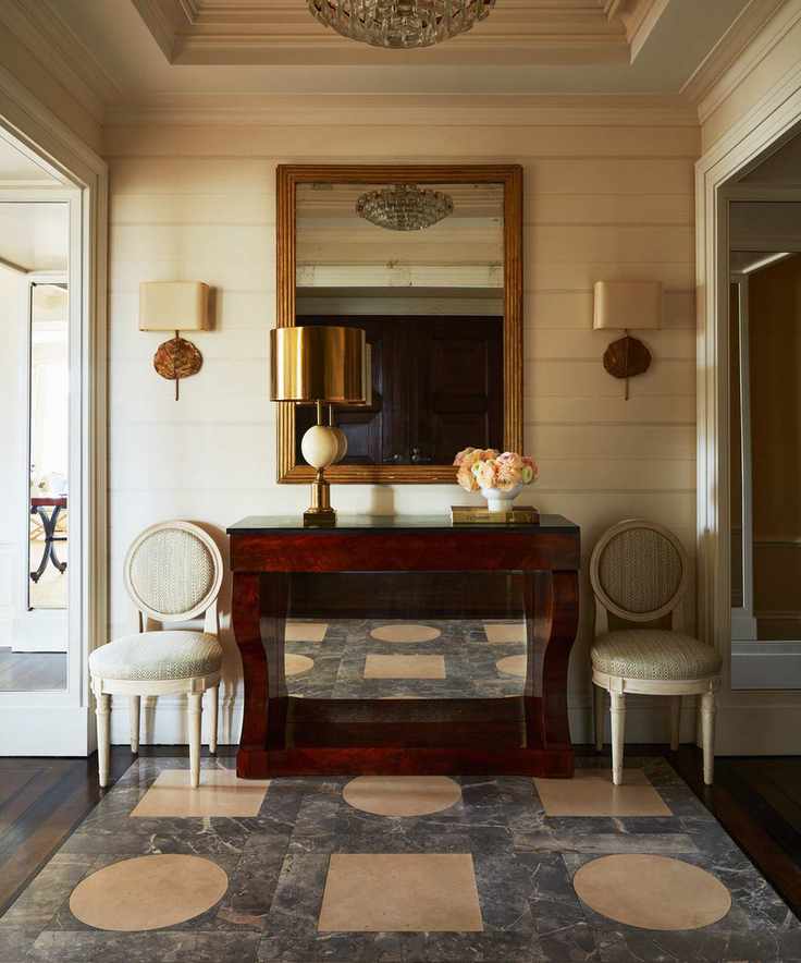 Classic entryway with symmetry, tiled floor, cream walls, and wall lights