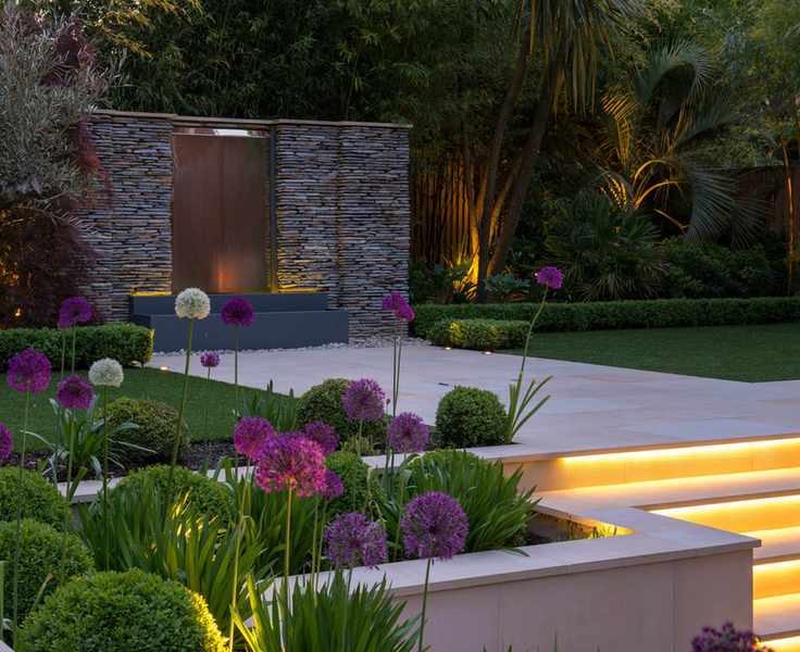 sleek water feature, pale paving and lit steps in a luxury garden design