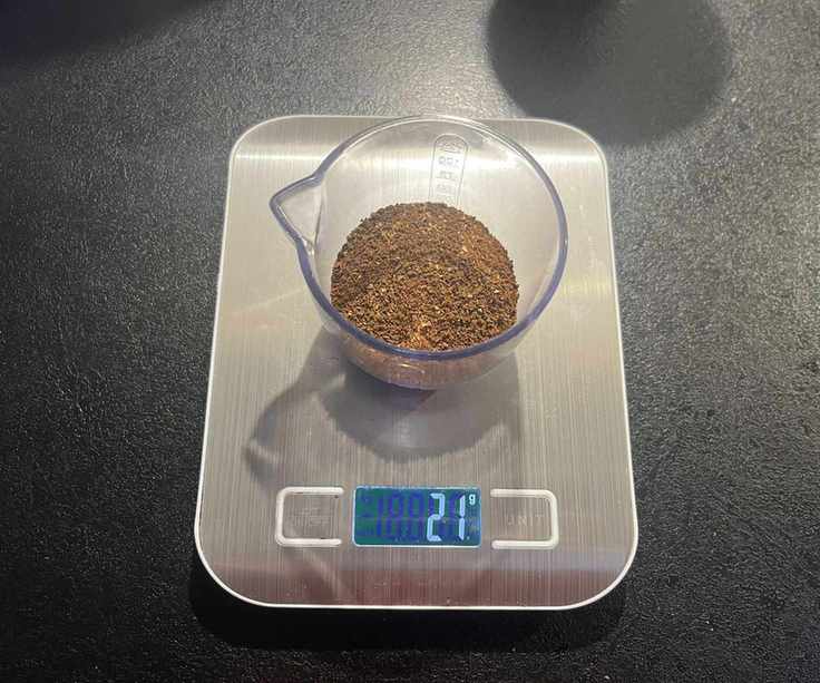 Medium ground coffee beans in a clear plastic container on digital weight scales.