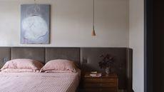 A mid-century style bedroom with a large brown headboard, a wooden nightstand, and a red and white striped bedding set