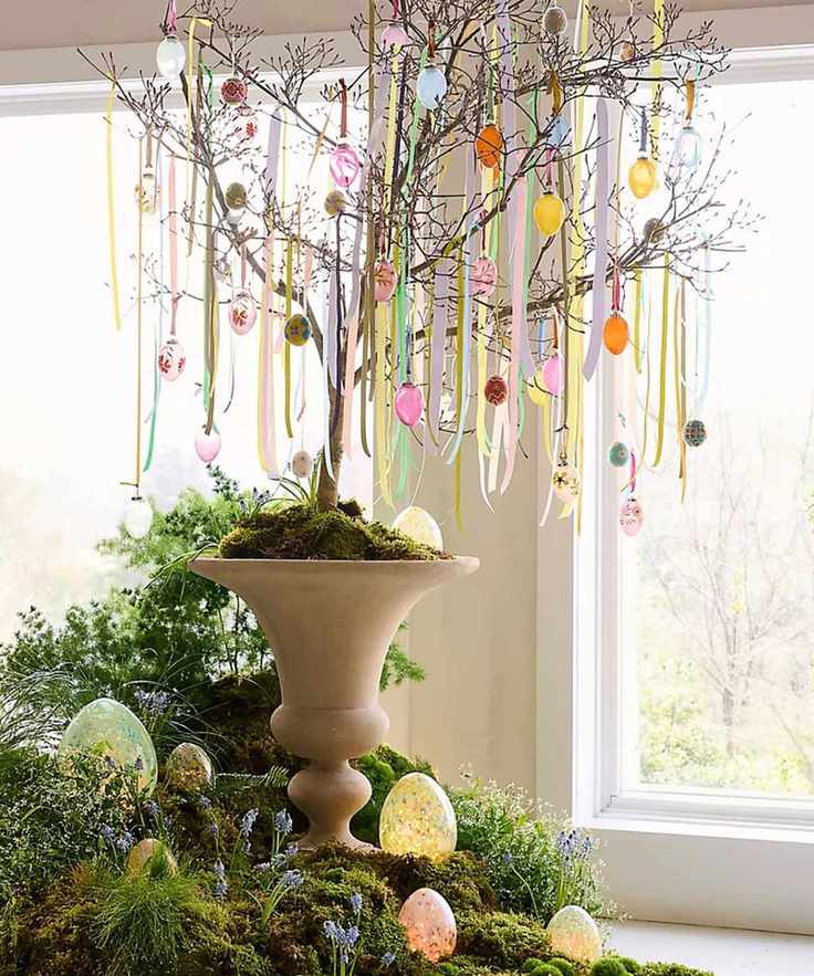 Large tree potted in an urn with a branchy tree decorated for Easter with eggs and ribbon with the base surrounded by moss and eggs