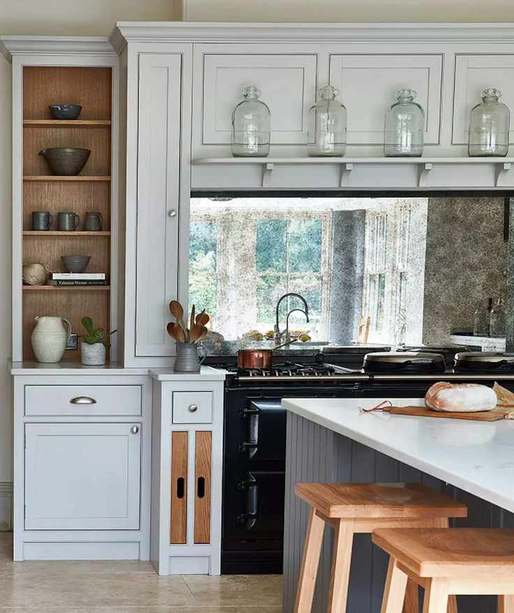 A country style kitchen with a black range cooker below a mirrored backsplash and light gray cabinets