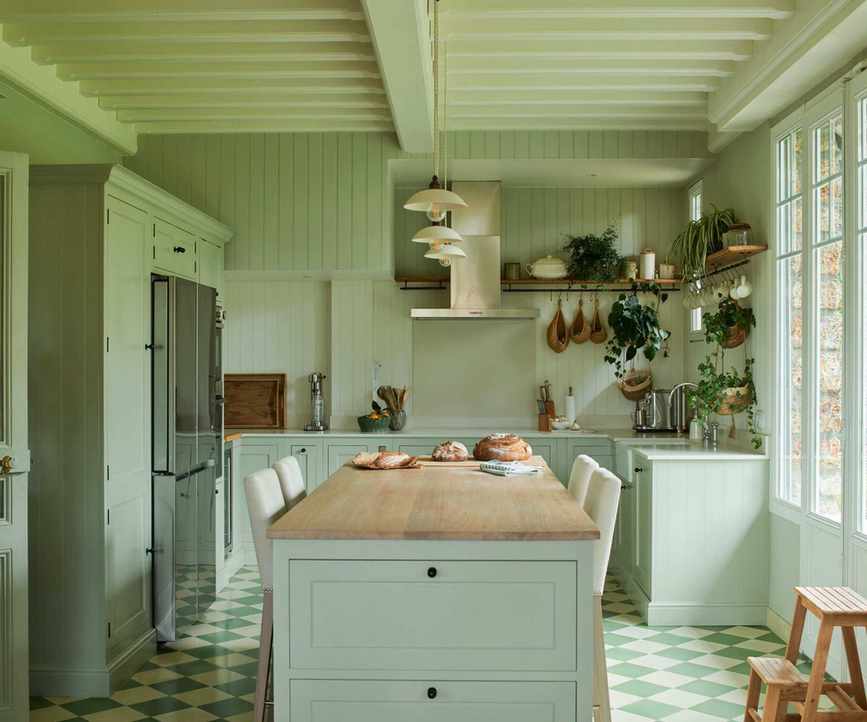A pale green color-drenched kitchen with a wooden island countertop, a stainless steel range hood, and green and white checkerboard tiled flooring.