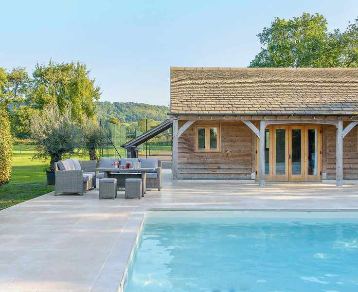 Timber-framed garden room adjacent to a swimming pool in a large garden.
