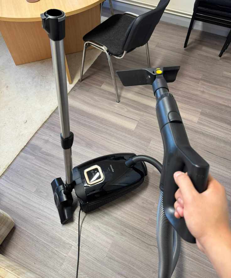 Miele Guard L1 Cat and Dog on wooden floor with handheld upholstery attachment.