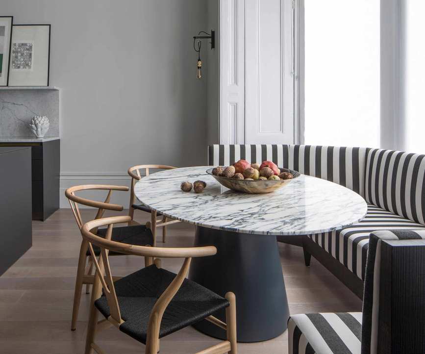 Breakfast nook created in a bay window with stripy upholstered banquette seating