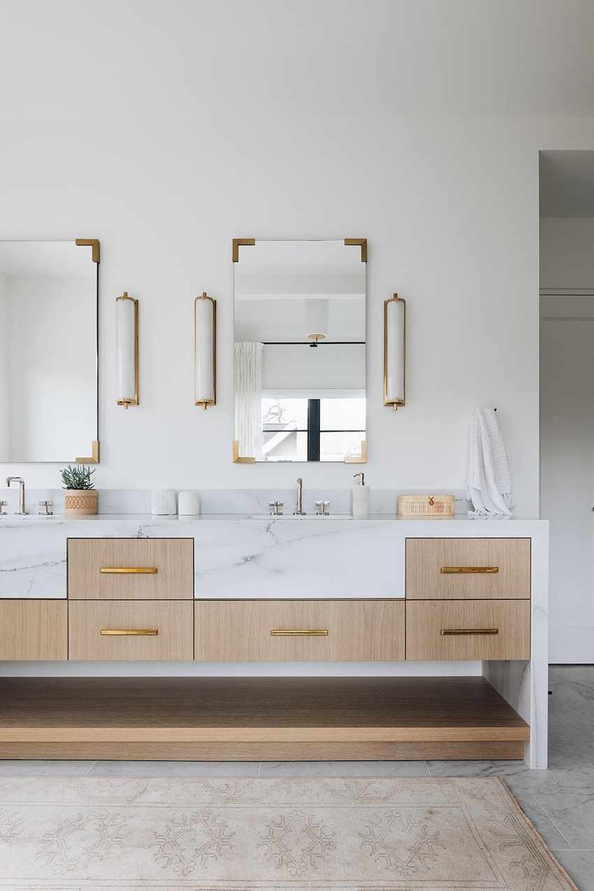 White modern bathroom with his and hers sinks, marble countertop, and light wood drawers.