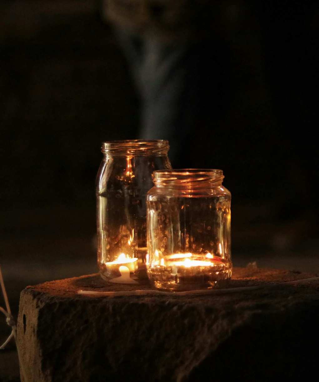 Two large mason jars with tea lights inside, sitting on a stone slab at dusk
