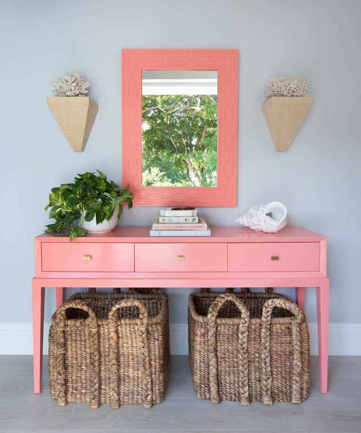 Entryway with painted pink console and matching mirror, rattan baskets, stack of books and potted plants
