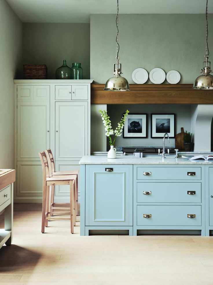 A baby blue kitchen island in a pale gray scheme with wooden bar stools, marble countertops and pale wooden flooring.