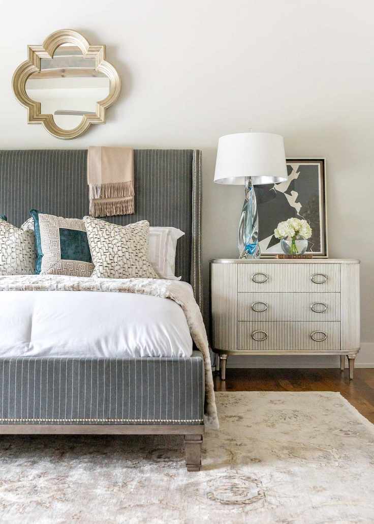 white bedroom with grey upholstered stripe bed, with bedding, rug, wooden floor, vintage bedside