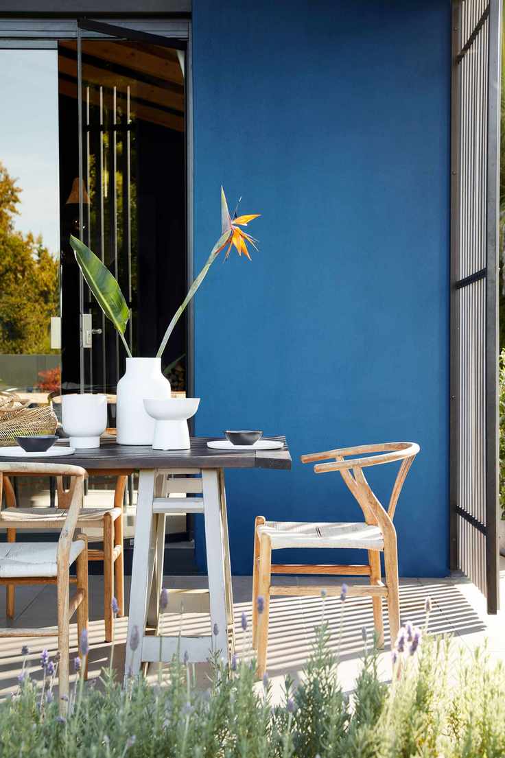 Mid-century wooden patio furniture ideas set against a bright blue painted wall.