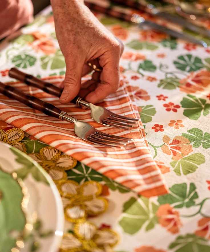 A close-up of a hand placing forks onto an orange striped napkin