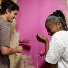 Two individuals painting a wall pink, enjoying the process