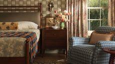 cozy cottage bedroom designed by Heidi Caillier for Lulu and Georgia with checked wallpaper, floral curtains, plaid chair and wooden bed and nightstand