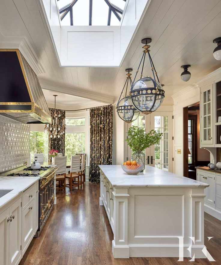 Large white kitchen with kitchen island, dark wooden flooring, open plan with dining room, large windows, dressed with dark patterned curtains
