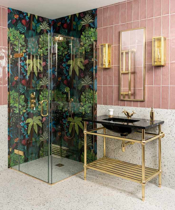 An example of bathroom shelf ideas showing a pink-tiled bathroom with walk-in shower clad with tropical patterned wallpaper, and an open gold vanity unit