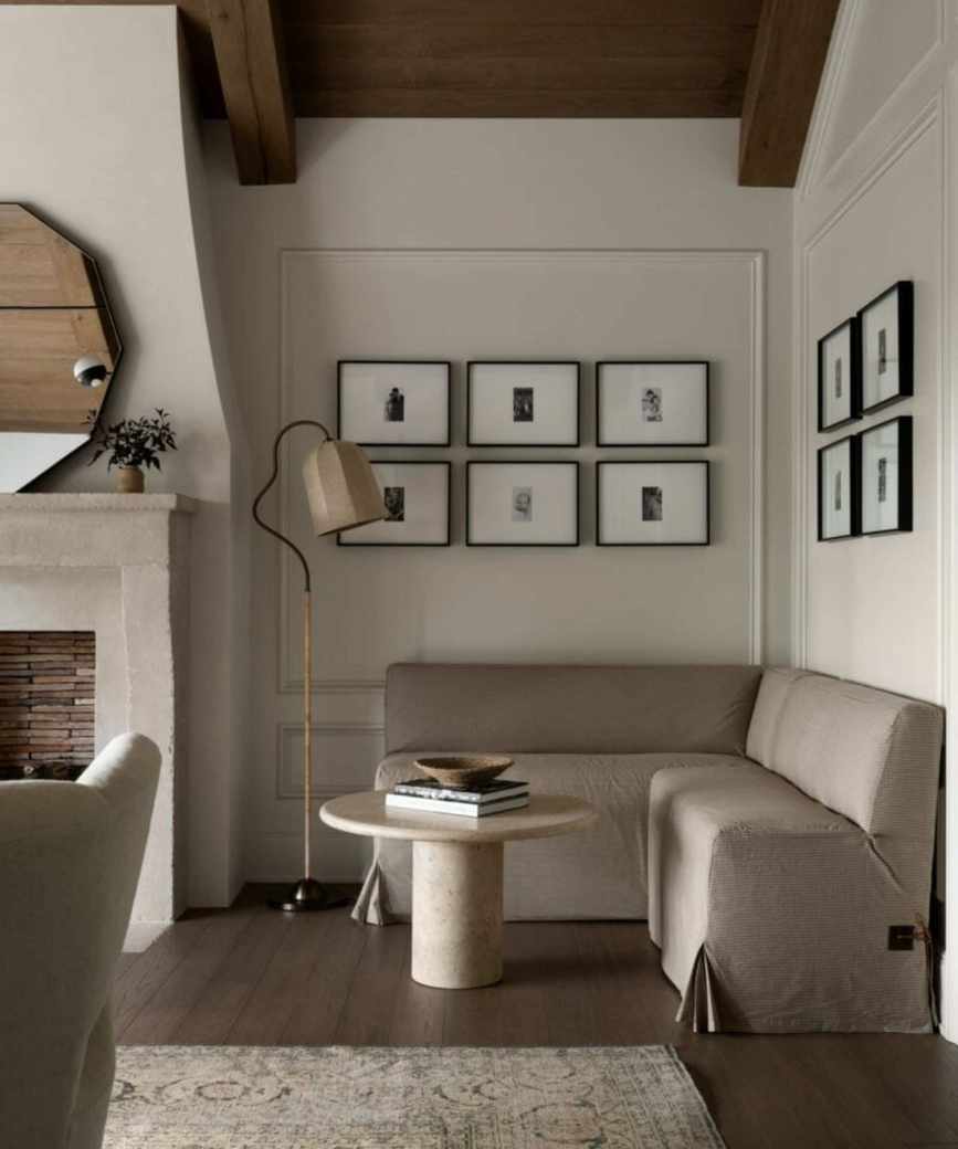 neutral rustic and moody bedroom designed by studio mcgee with a fireplace and a corner banquette seat in neutral linen upholstery styled with a small marble table with a stack of books