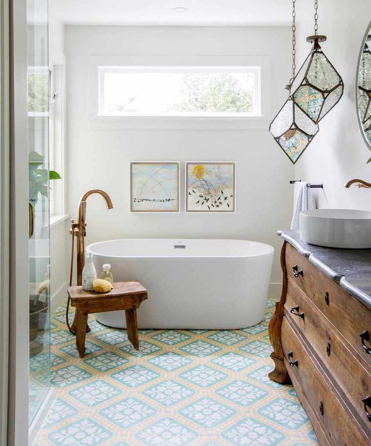 narrow bathroom ideas, patterned tiles on floor, bath, vintage stool and sideboard, brass standpipe, glass pendants