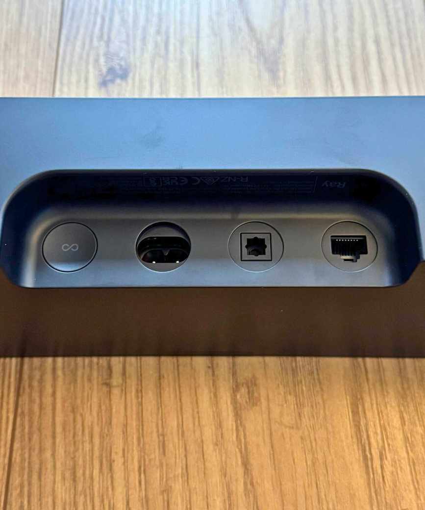 Closeup of the Sonos Ray soundbar's cable ports and button, on wooden floor.