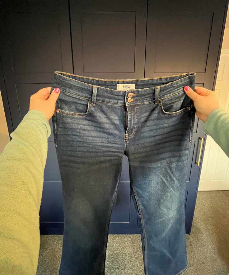 Pictured is a pair of jeans being held in front of the camera person's view with one hand on the left and right side of the waistband