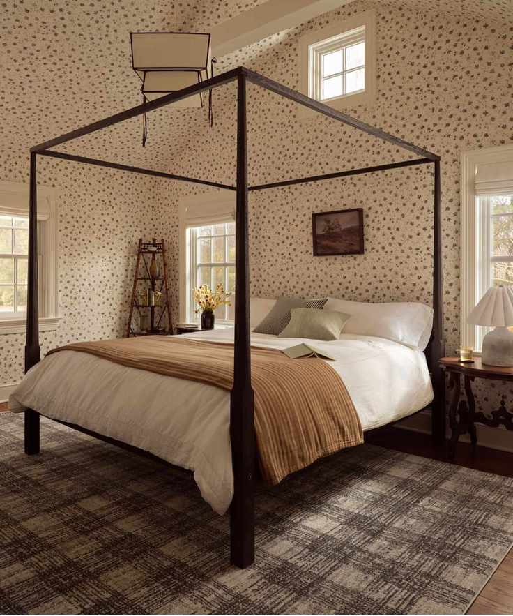 bedroom with black four posted bed, ditsy floral walls and ceiling with a neutral and beige styled bed and a plaid grey brown rug underneath