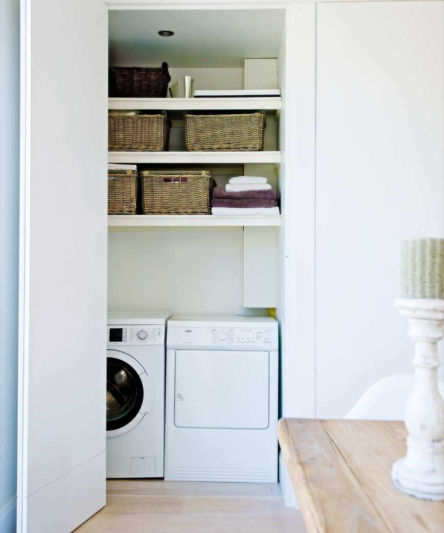 A laundry room with washing machine and dryer and shelves above with wicker baskets