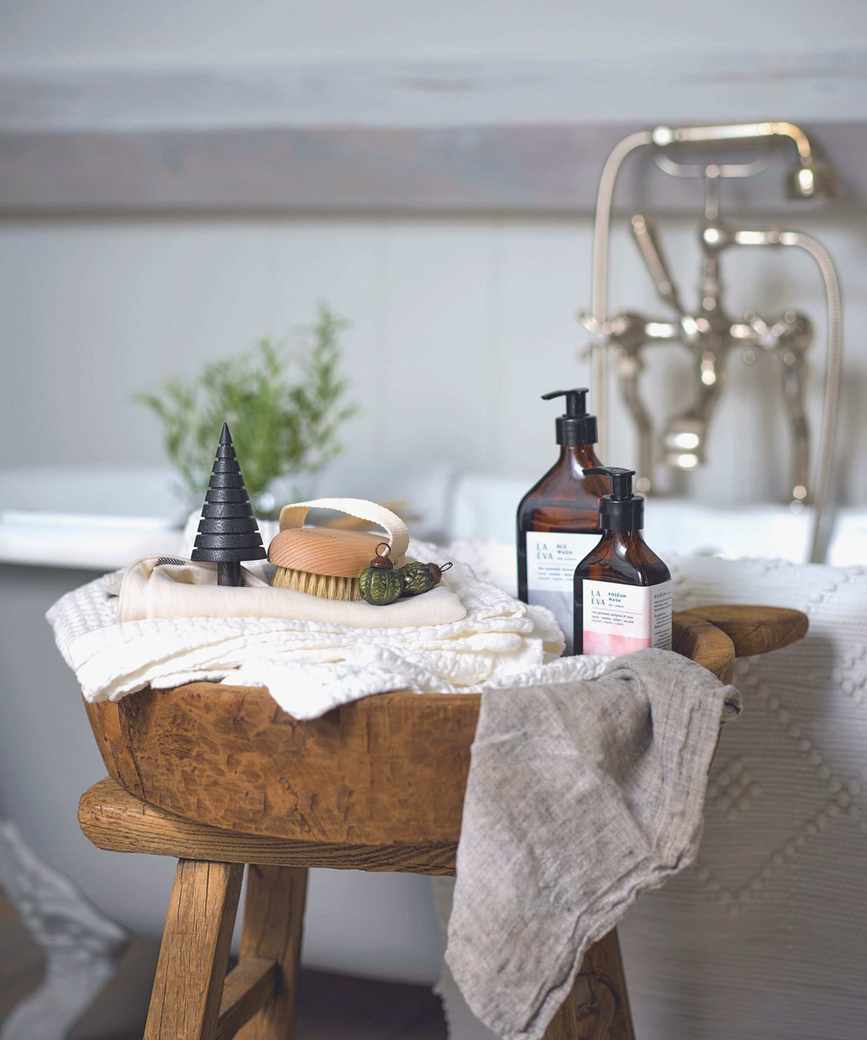 Wooden bowl with toiletries and towels on a wooden stool, grey roll-top bath in the background