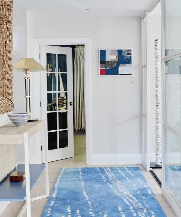 A white entryway featuring a blue and white rug and an open door leading to another room.