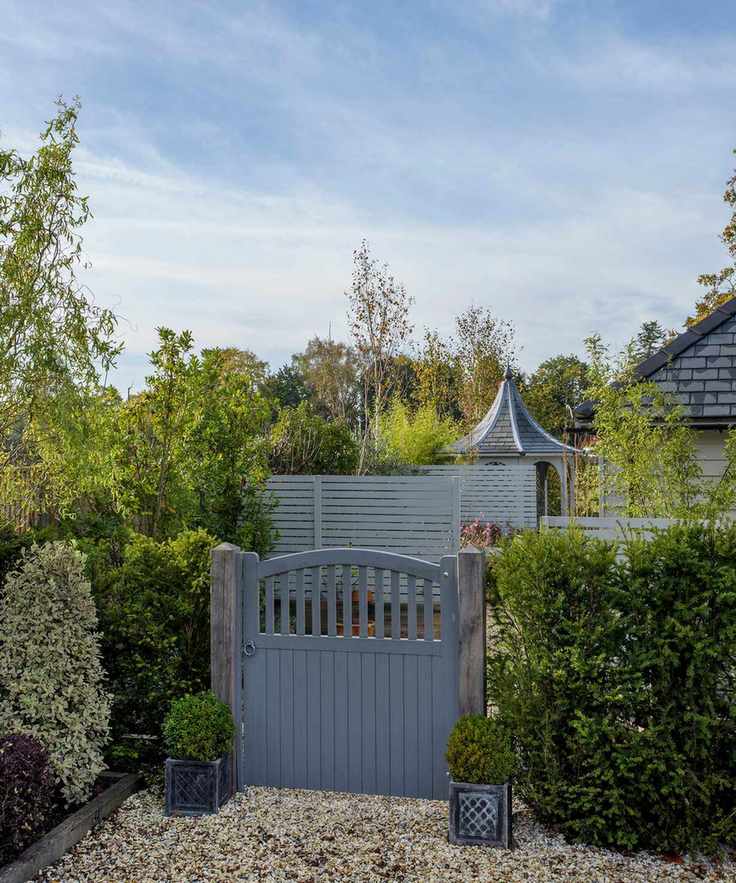 A gray painted wooden gate surrounded by hedges, with gravel flooring.