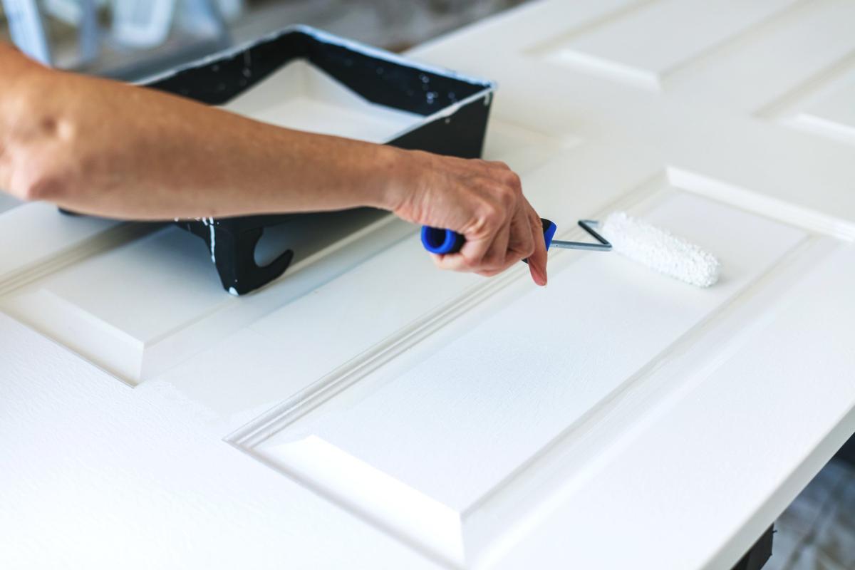 A hand using a small roller to paint a door white