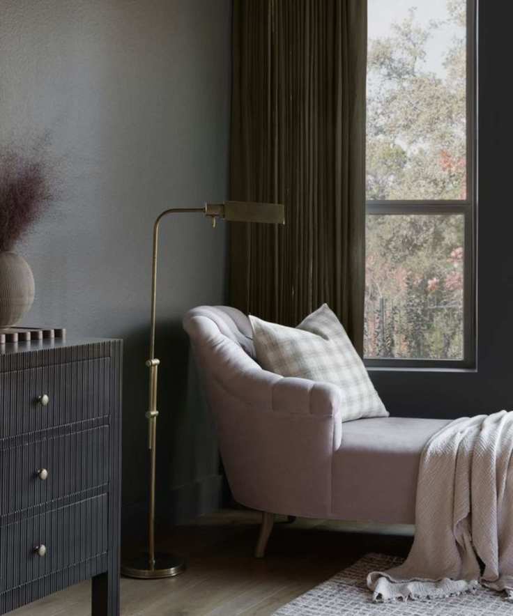 a corner of a room with grey walls, a pink chaise longue, and a gold contemporary floor lamp