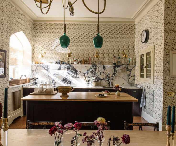 bright and open kitchen with floral wallpaper and a dark painted kitchen with purple veined marble counters and backsplash