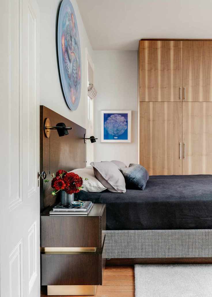 A Mid-Century modern style bedroom with a large wooden headboard, a nightstand with gold accents, and a bed made with a blue velvet throw