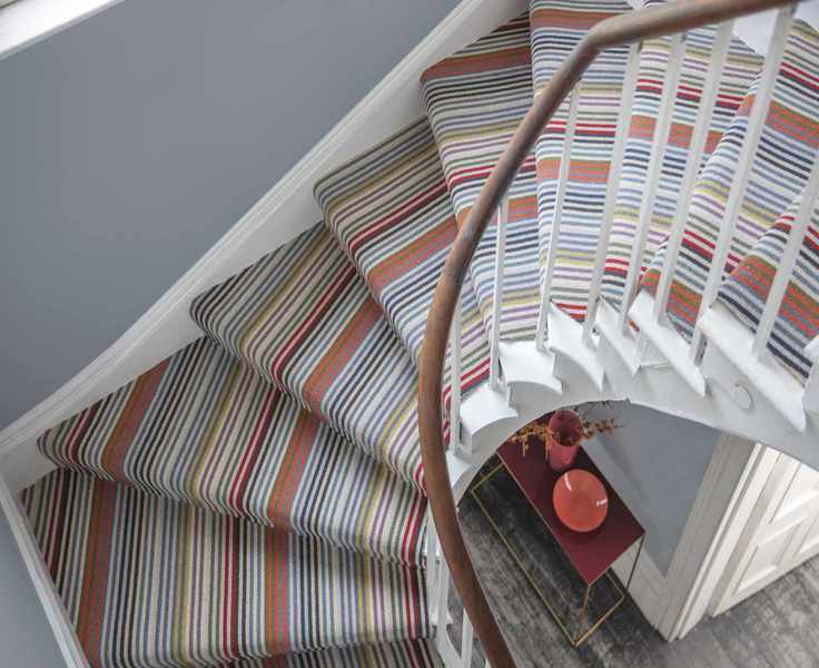View of curved staircase from above with grey wall and striped carpet
